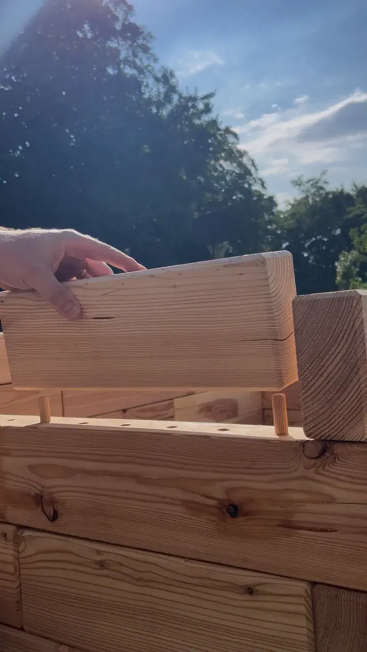 A hand placing a larch piece onto wooden dowels while building a raised garden bed