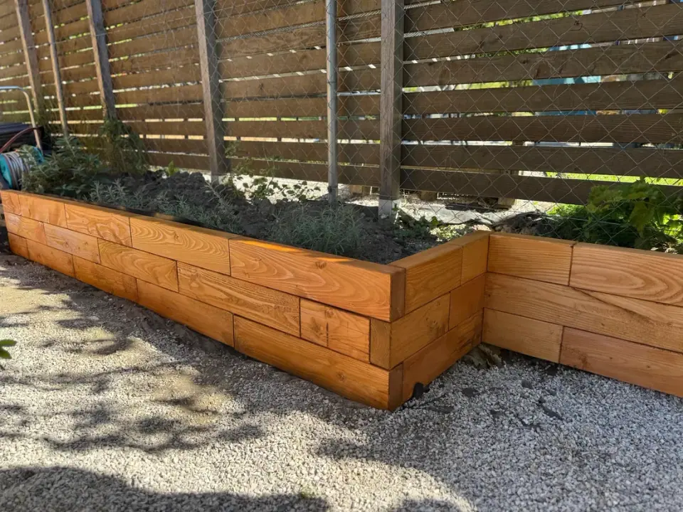 L-shaped raised bed made of larch pieces by a wooden fence
