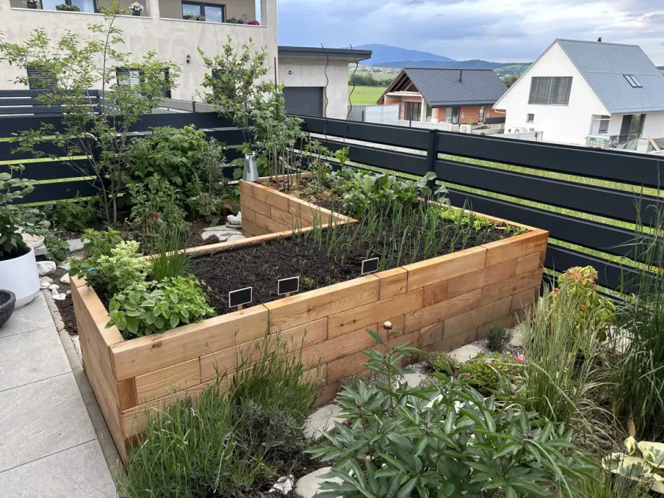 L-shaped raised garden bed made of larch pieces with plants on the terrace of a family house