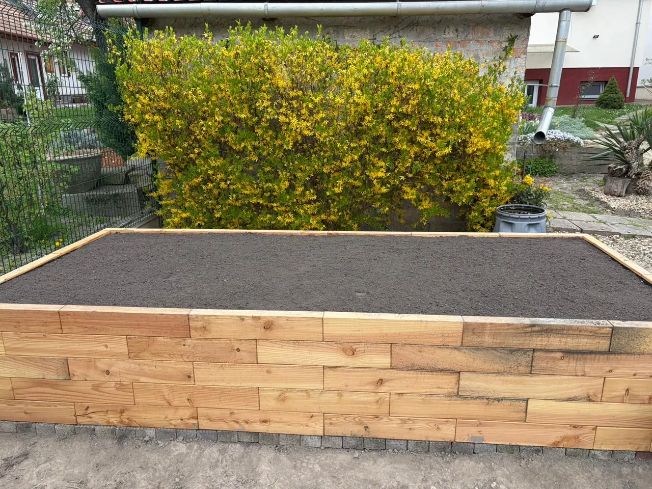 Strat înălțat Brick Premium plin cu pământ în fața unui arbust înflorit